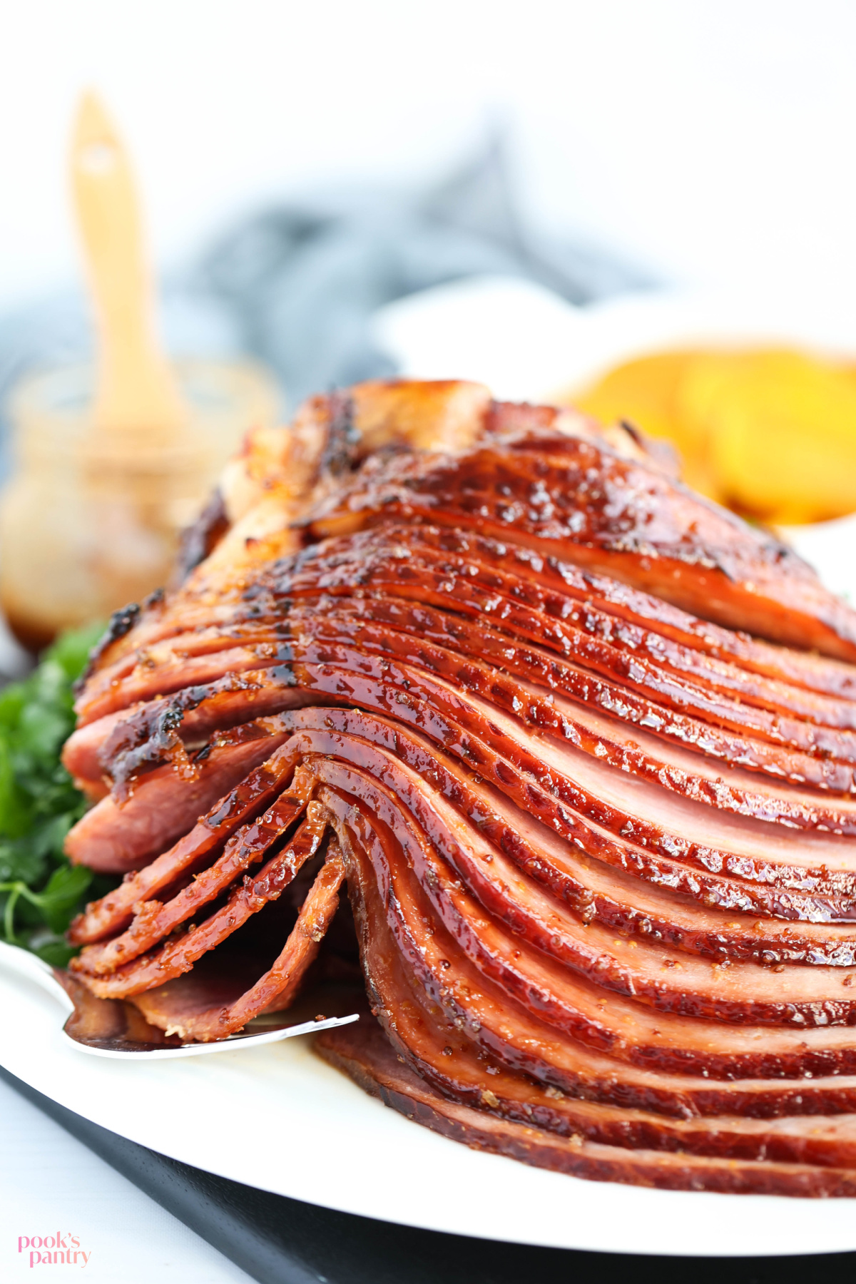 Slices of honey chipotle glazed ham on a white serving platter, with golden beets in a casserole dish in the background.