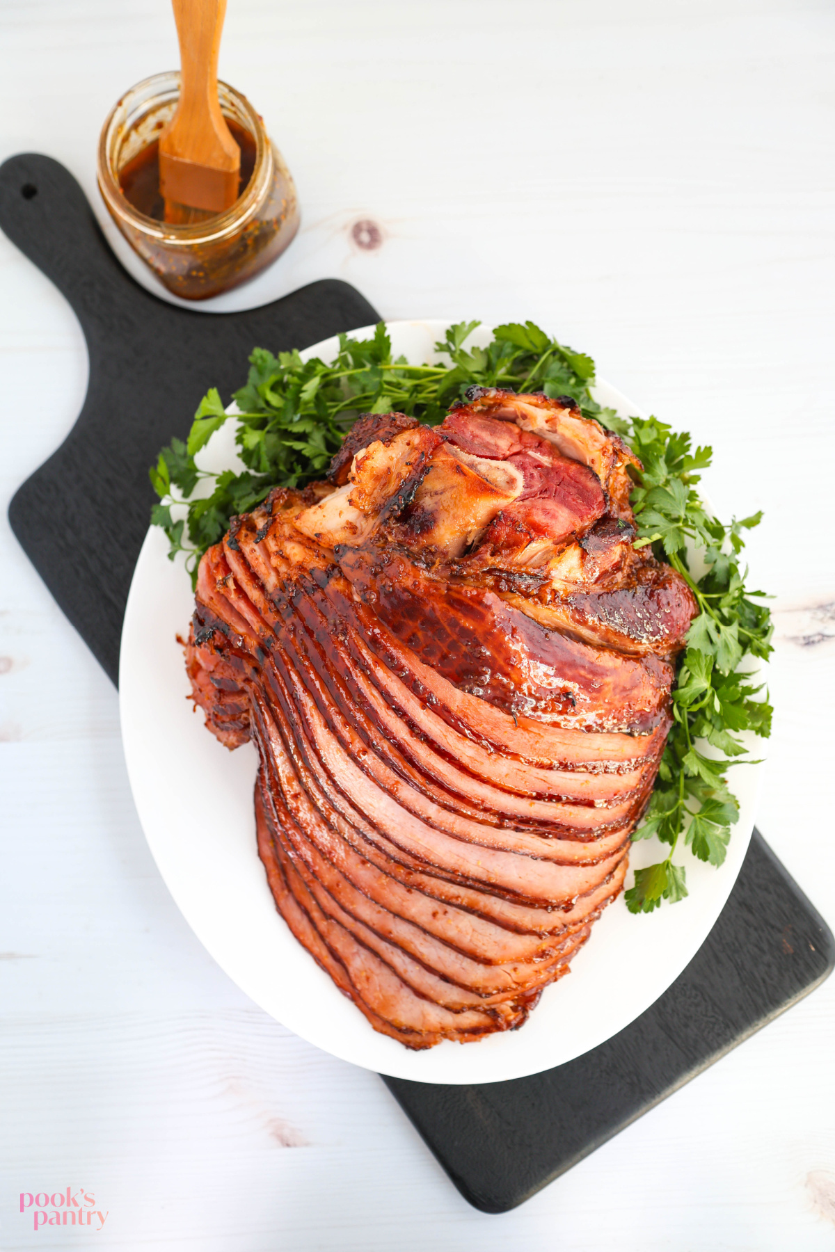 Overhead photo of glazed, spiral-sliced ham on a white serving platter with parsley on the side.
