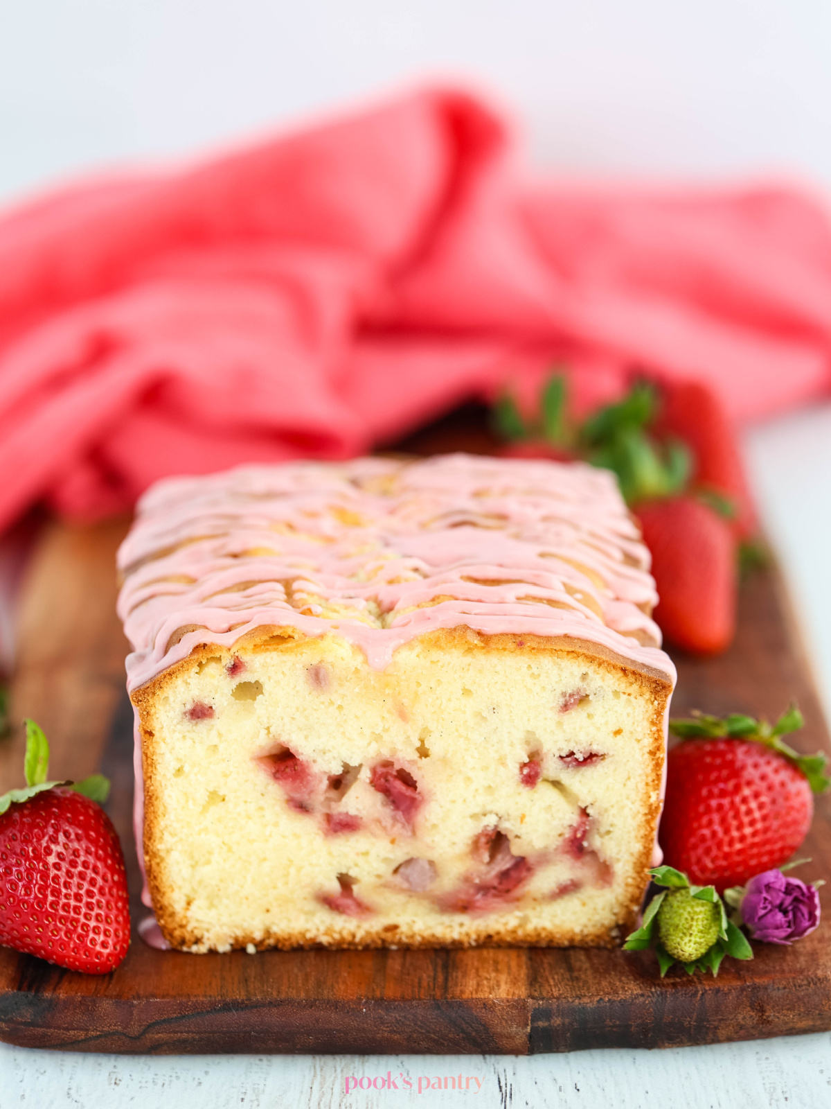 Pound cake with strawberry glaze on top. The cake is on a brown wooden board, with strawberries on the side.