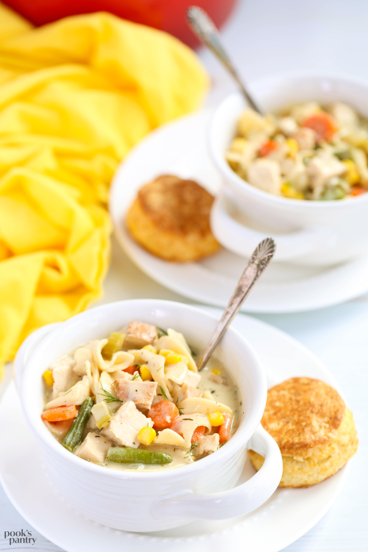 Bowls of soup sitting on small white plates with a homemade biscuit on the side.