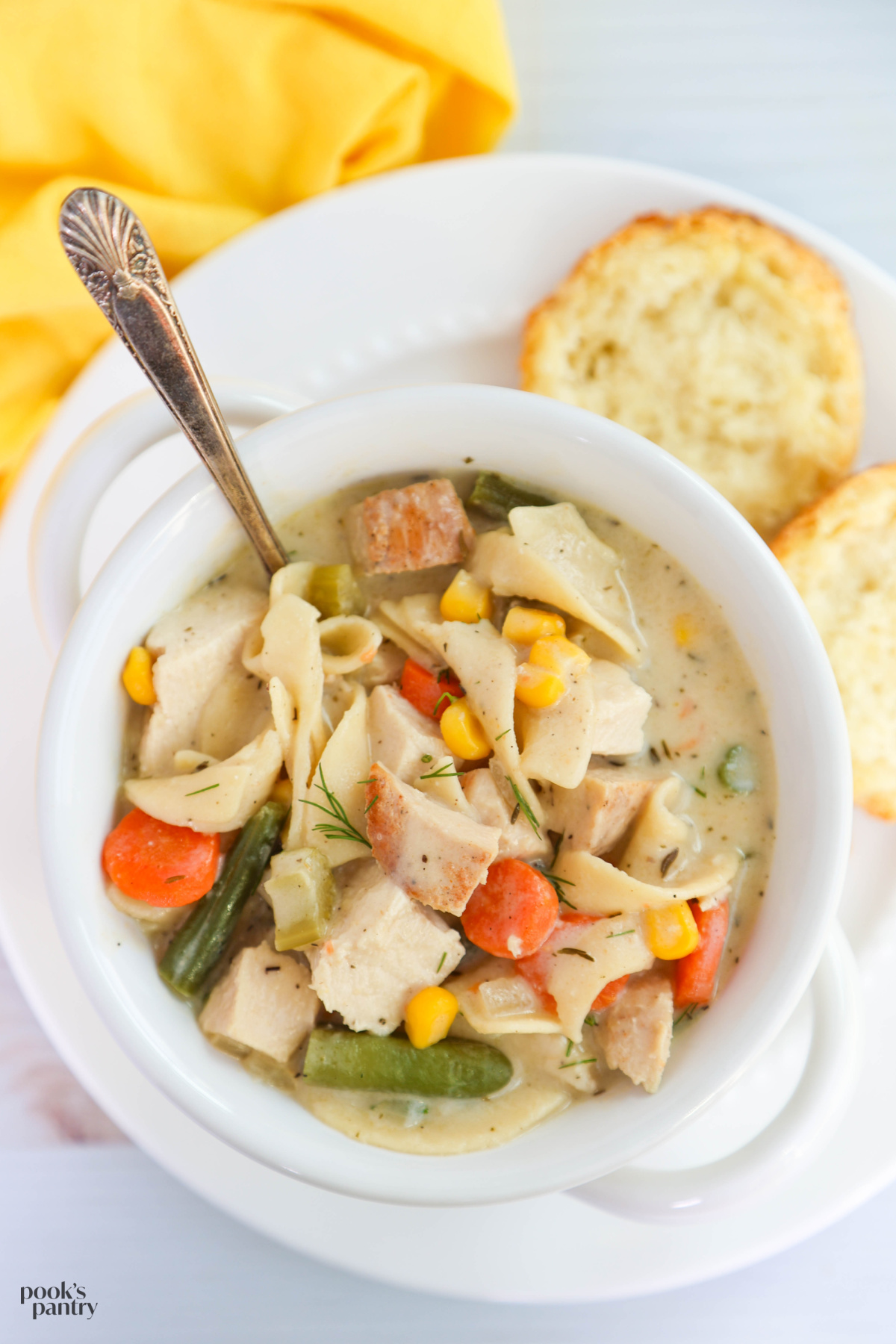 Chicken vegetable noodle soup in a bowl with a biscuit on the side.