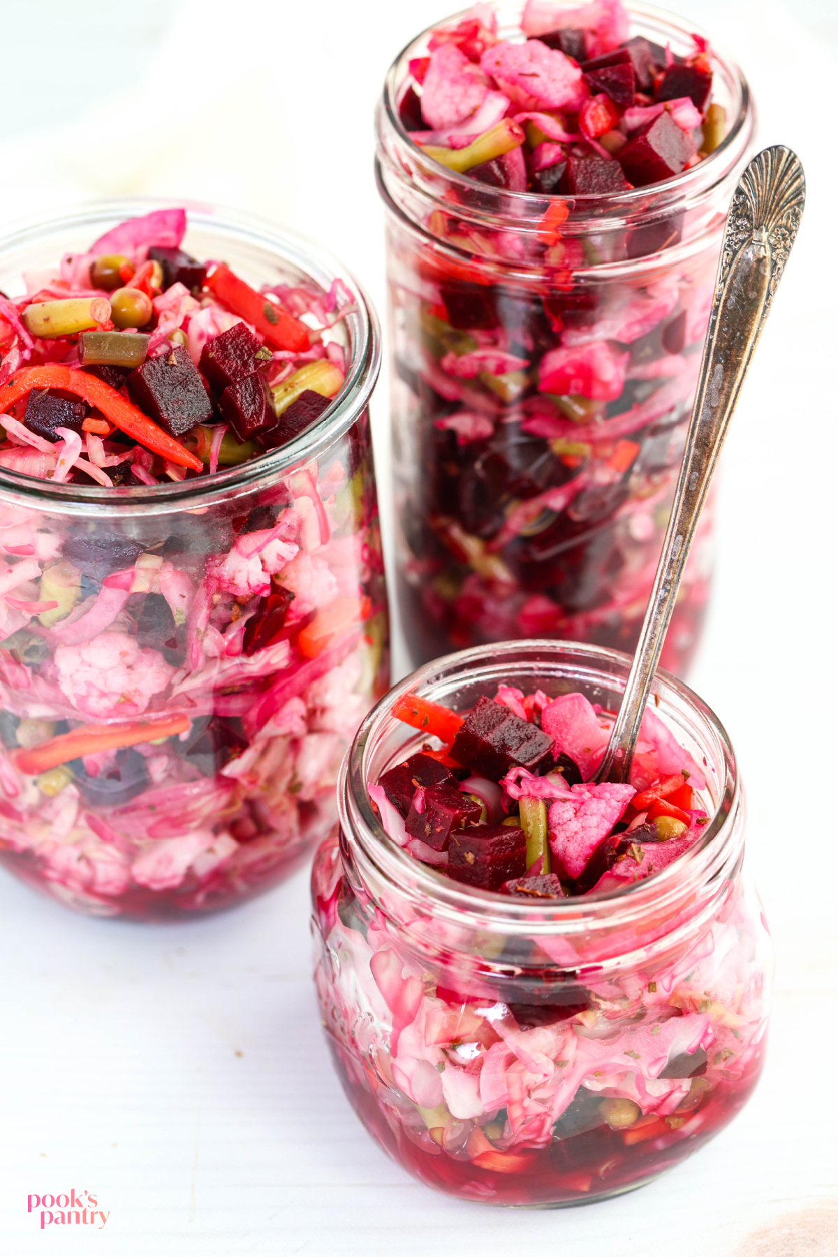 Jars of various sizes filled with beet curtido on a white background.