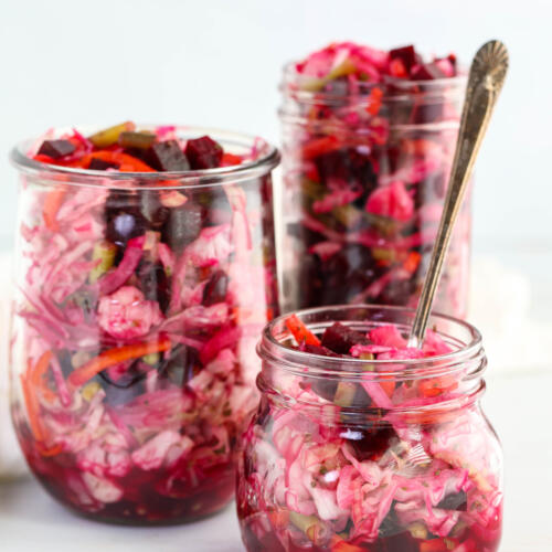 Glass jars filled with a Guatemalan curtido recipe. The jars are different sizes, and the smallest jar has an antique fork in it.