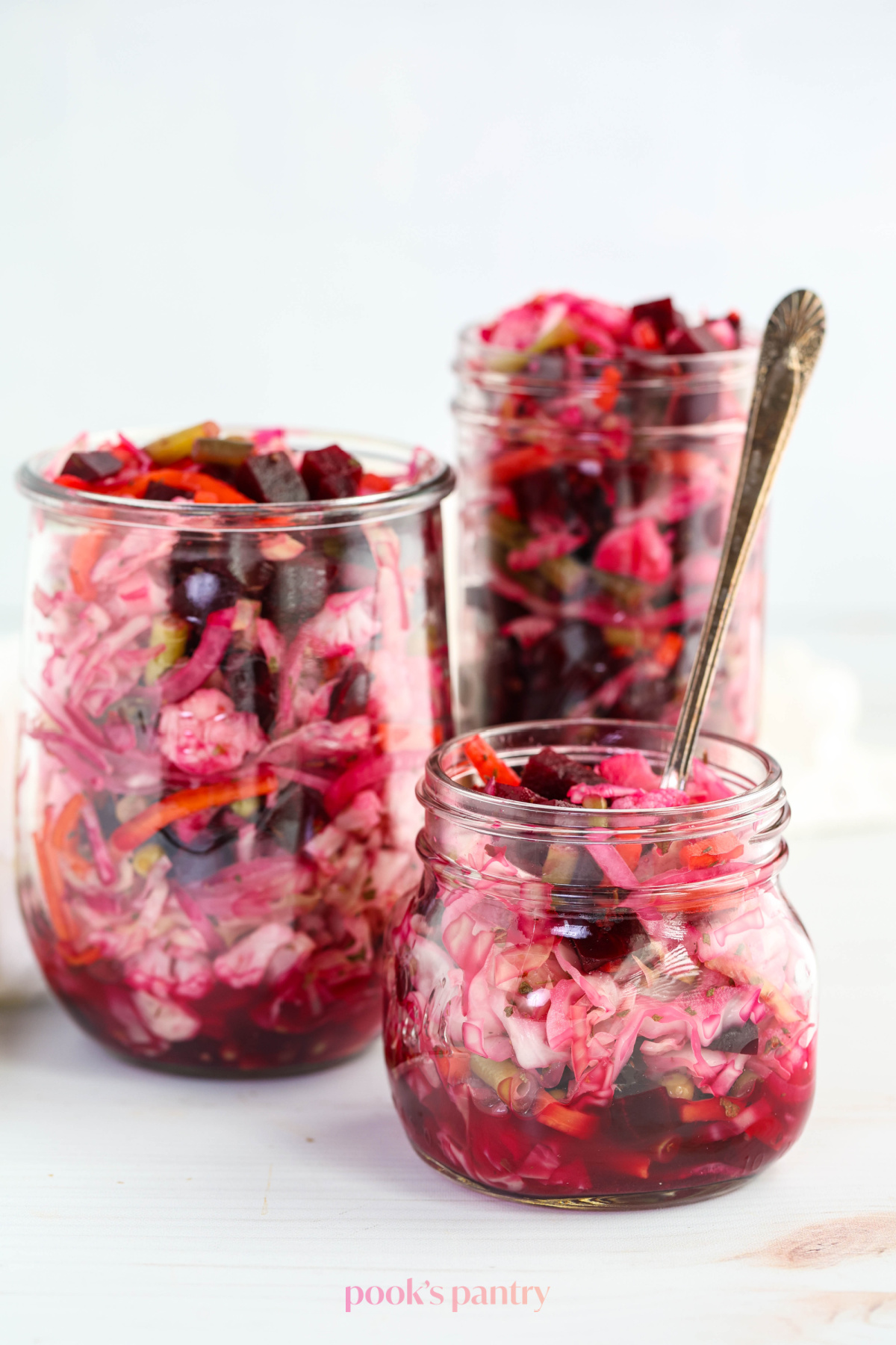 Glass jars filled with a Guatemalan curtido recipe. The jars are different sizes, and the smallest jar has an antique fork in it.