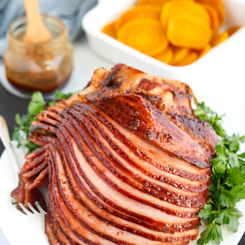 Honey mustard glazed ham recipe on a white platter with parsley on the side.