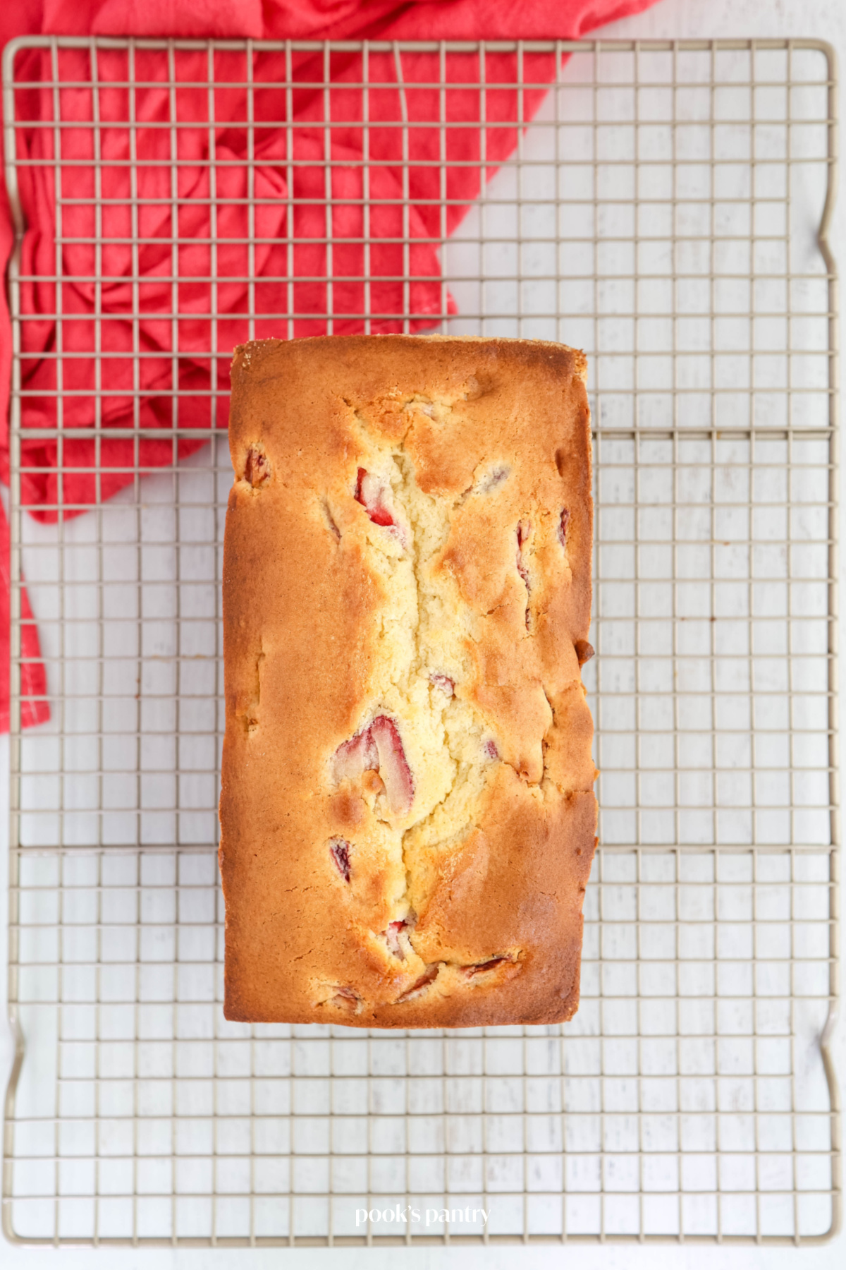 Freshly baked pound cake on a cooling rack with a pink tea towel underneath the rack.