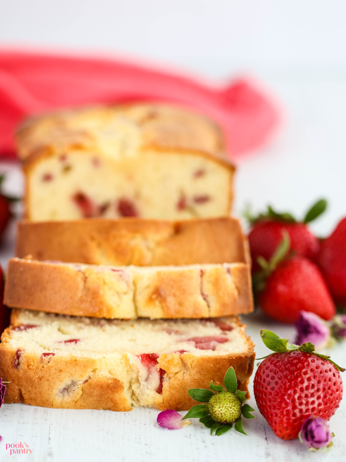 Slices of poundcake on a white background with fresh strawberries on the side.