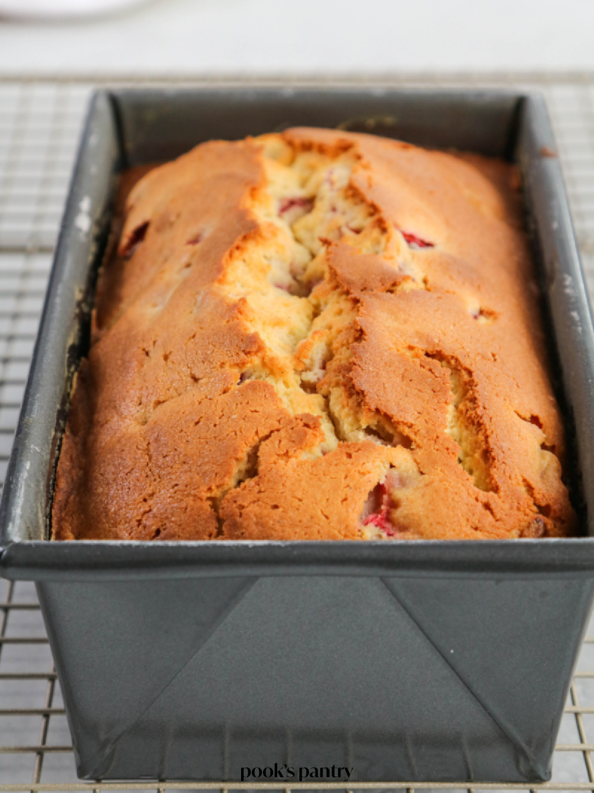 Strawberry cream cheese pound cake cooling in a loaf pan on top of a metal cooling rack.