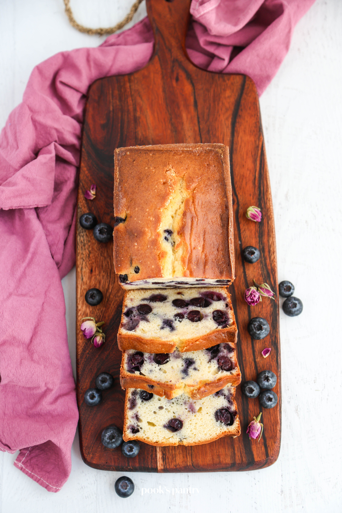 Pound cake with a few slices cut from it, laying on a wooden board, with a purple tea towel under the board.