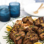 Grilled lamb loin chops with rosemary and lemon on a white platter with a blue and white background.