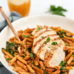 Chicken spinach pasta with sun-dried tomatoes in a wide shallow bowl with a fork.