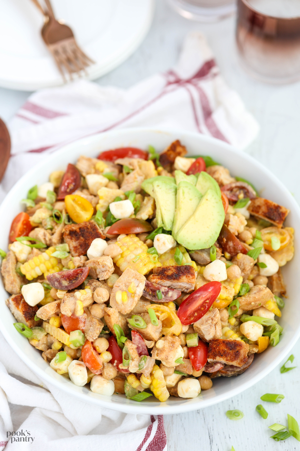 BBQ chicken chopped salad in white bowl with sliced avocado on top.
