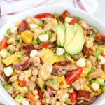 Barbecue chicken salad in a shallow white bowl with a tea towel beside the bowl.
