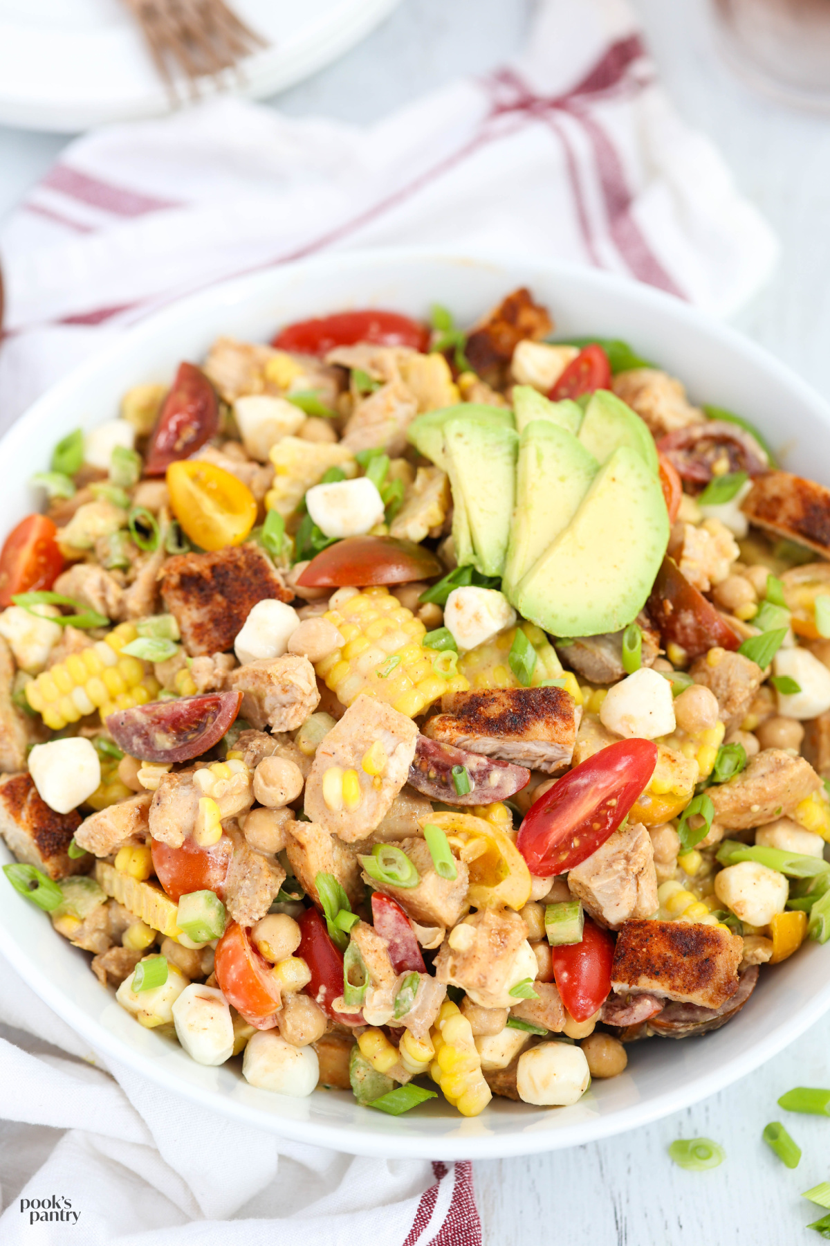 Barbecue chicken salad in a shallow white bowl with a tea towel beside the bowl.