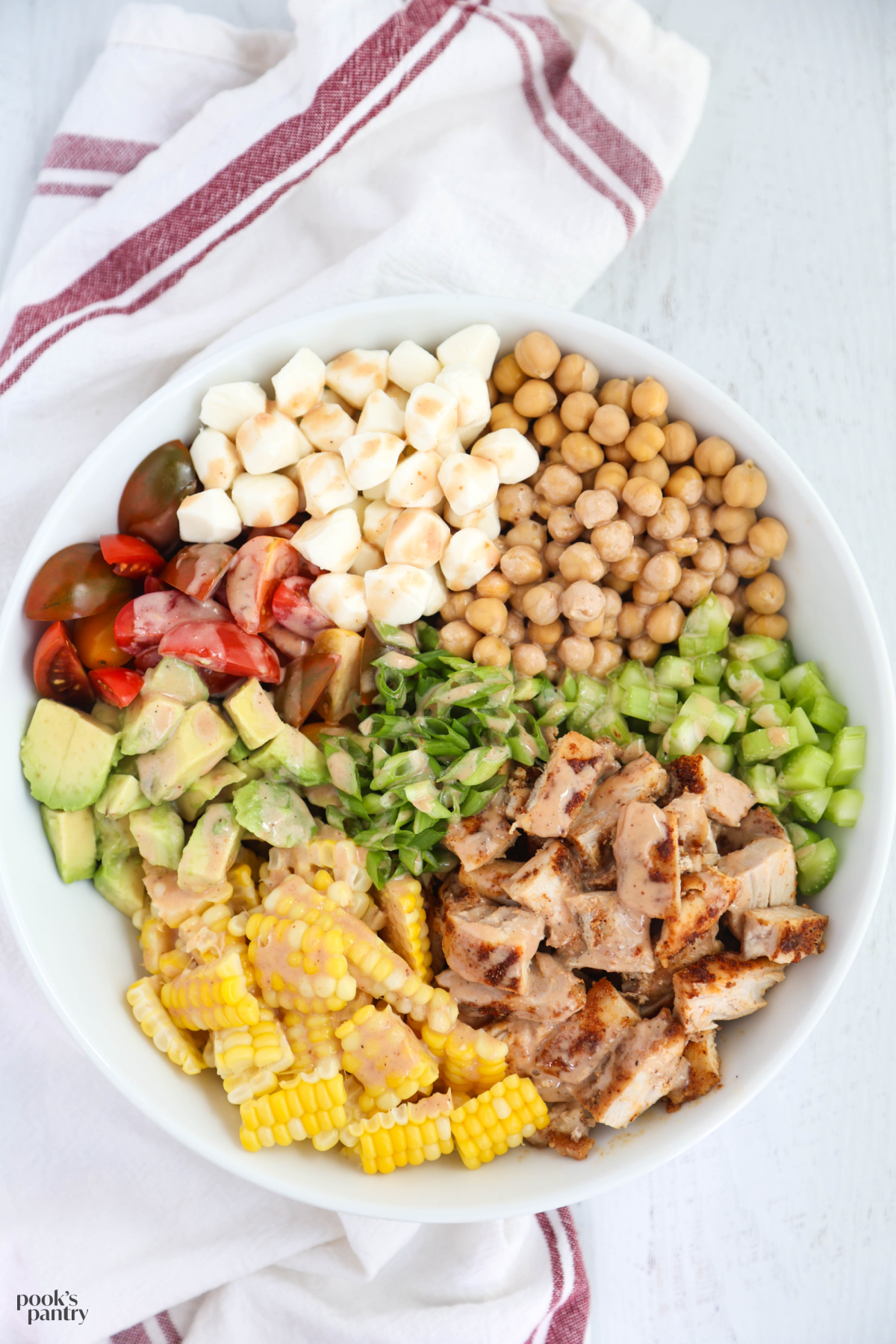 Chicken salad with tomatoes, avocado and corn drizzled with a barbecue dressing in a white bowl.