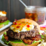 Goat cheese burger with bacon and pepper jam on a white plate with macaroni salad on the side.