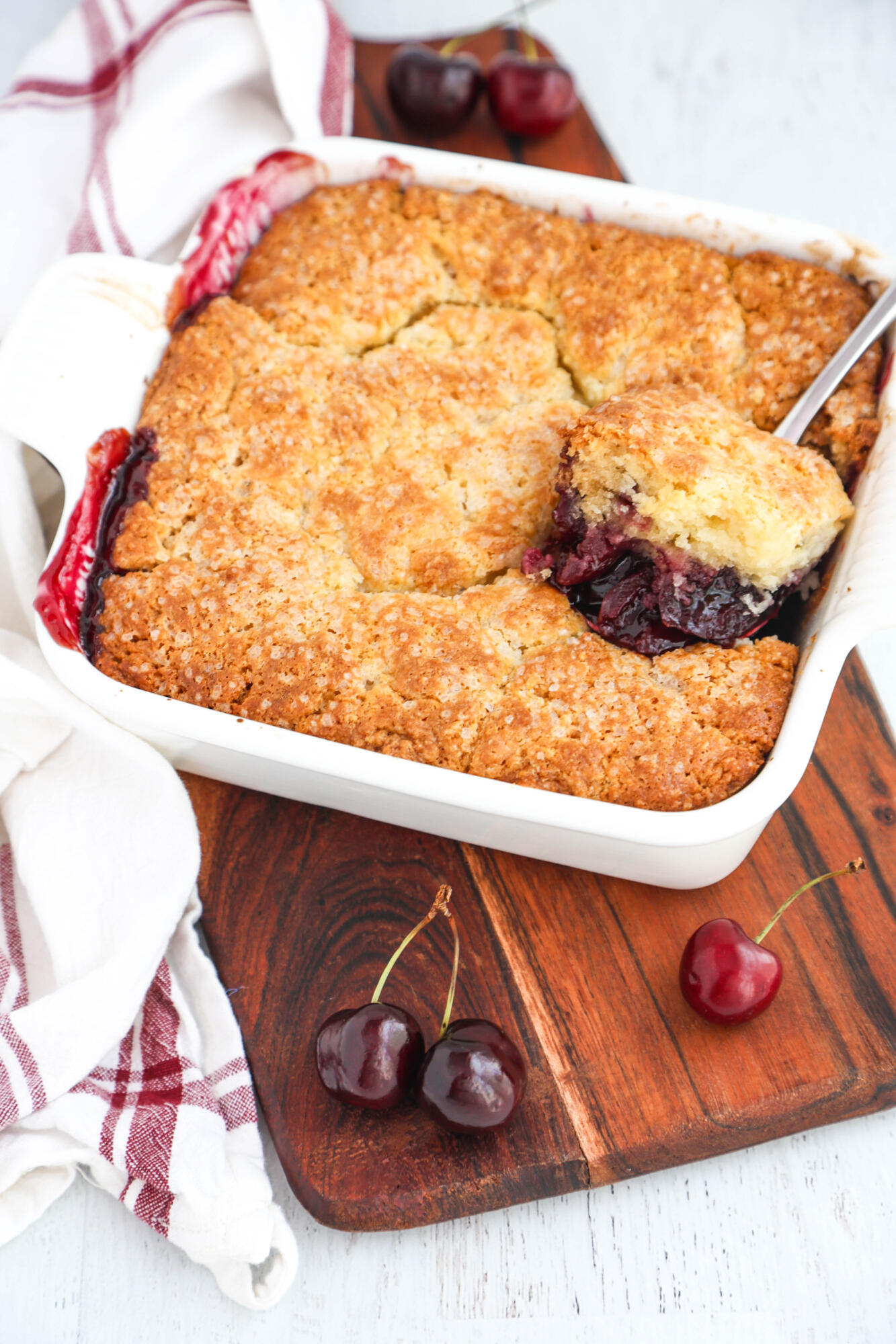 Scooping a spoonful of cobbler out of a baking pan sitting on a wooden board.