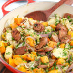 One pan chicken sausage and veggies in a red pan with a wooden spoon at the back of the pan.