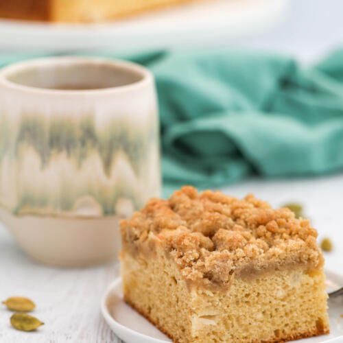 Pear coffee cake with cardamom crumble on a small white plate with a handmade coffee mug behind the plate.