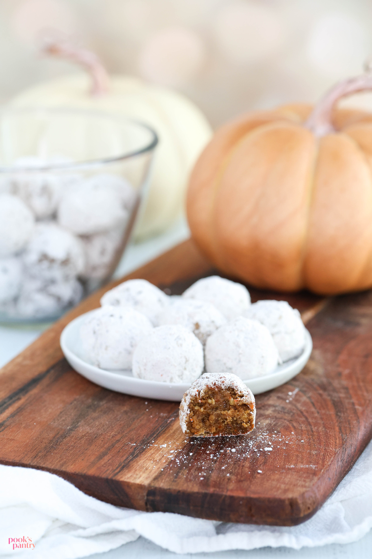 A pumpkin rum ball cut open to show interior sitting in front of a plate of rum balls on a wooden board.