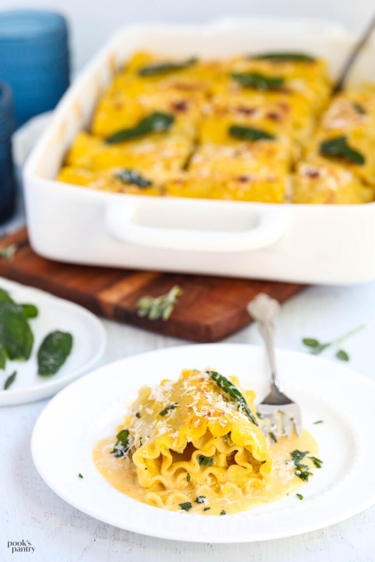 Hubbard squash lasagna roll ups on a white plate with fried sage leaves.