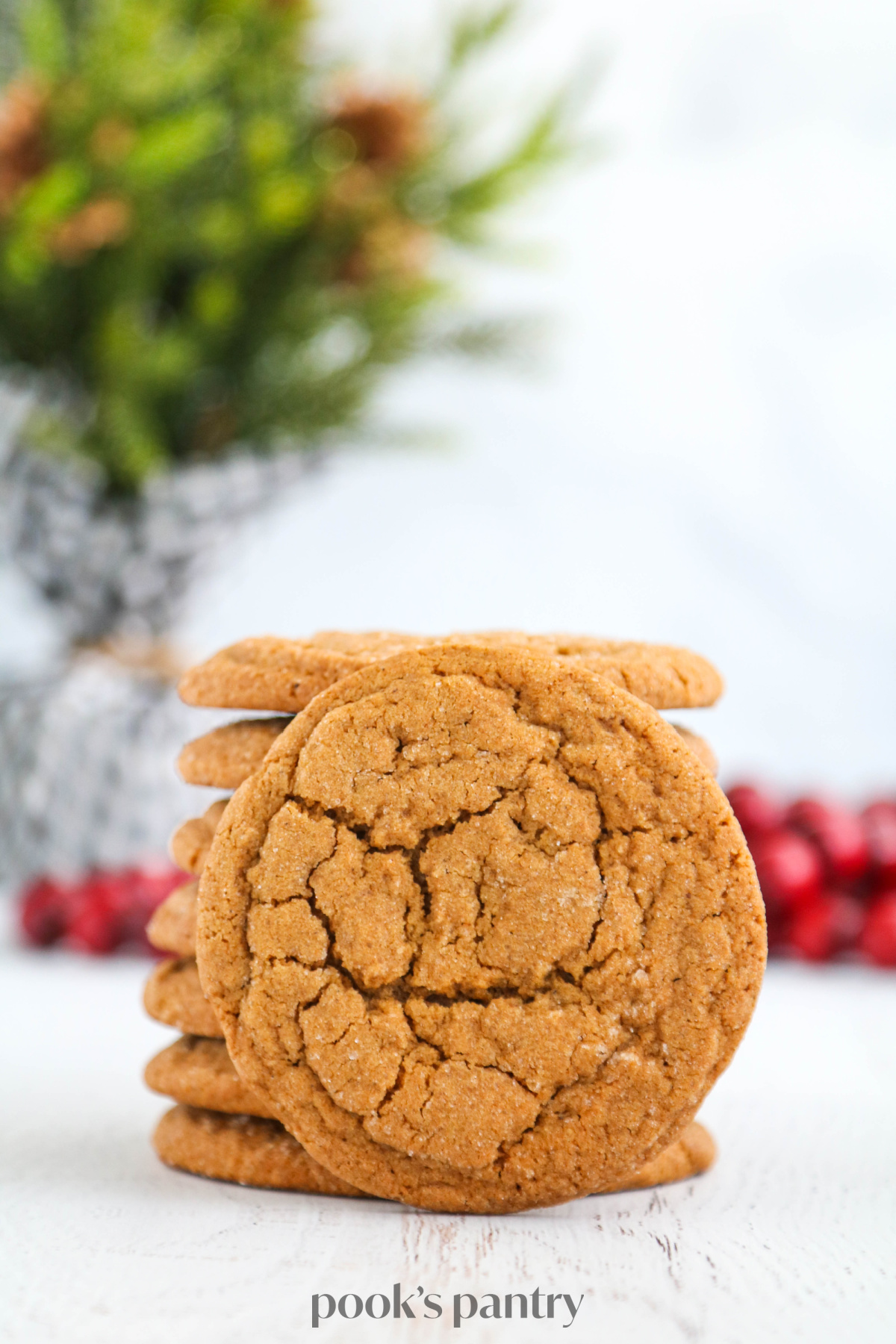 Ginger molasses cookies stacked on top of each other in front of wooden cranberry beads and a small evergreen tree.