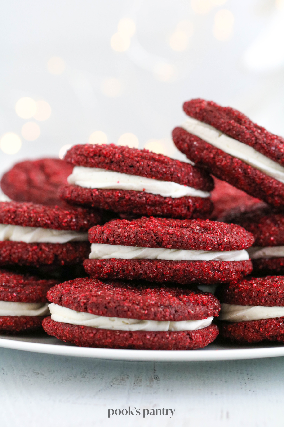 Sandwich cookies on a white platter in front on a white bokeh background.
