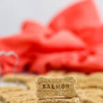Three ingredient homemade salmon dog treats stacked on top of each other in front of a dark pink towel.