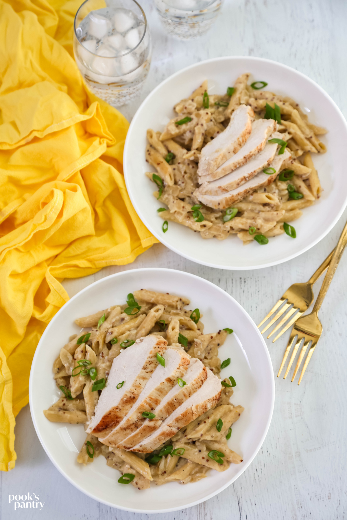 Overhead photo of two bowls of pasta and glasses of ice water with a yellow towel on the side.