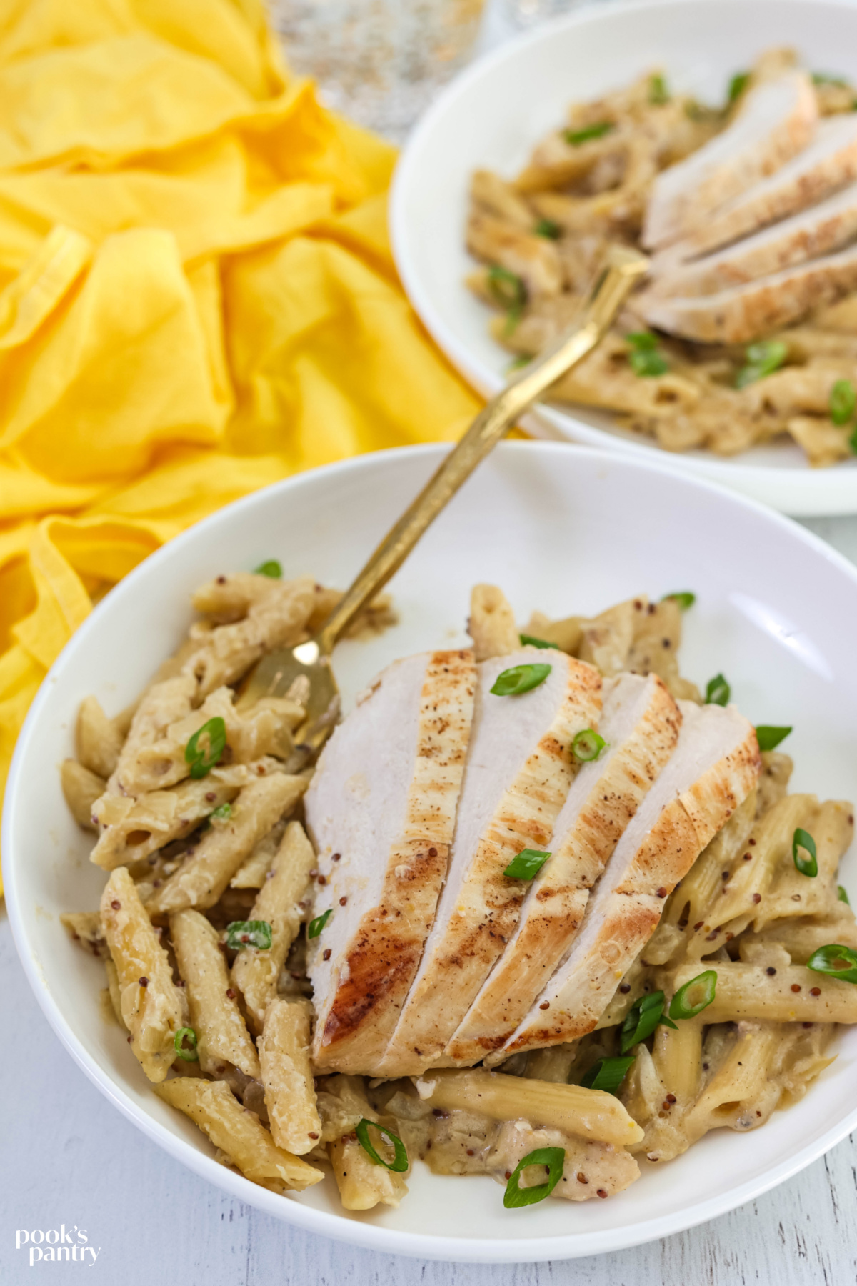 Chicken and pasta in shallow white bowls with a gold fork in the pasta.