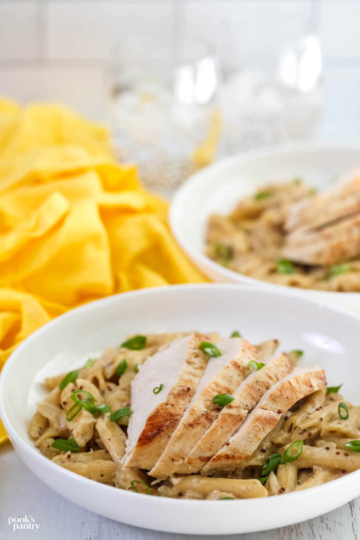 Sliced chicken on top of Dijon pasta in a bowl, with sliced scallions scattered on top.