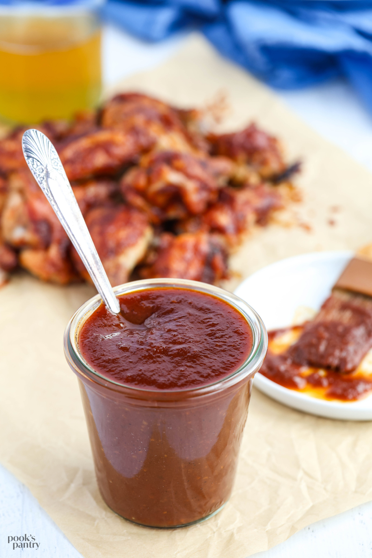 Maple bourbon BBQ sauce in a clear glass jar with an antique spoon in the jar. There are sauced wings in the background.