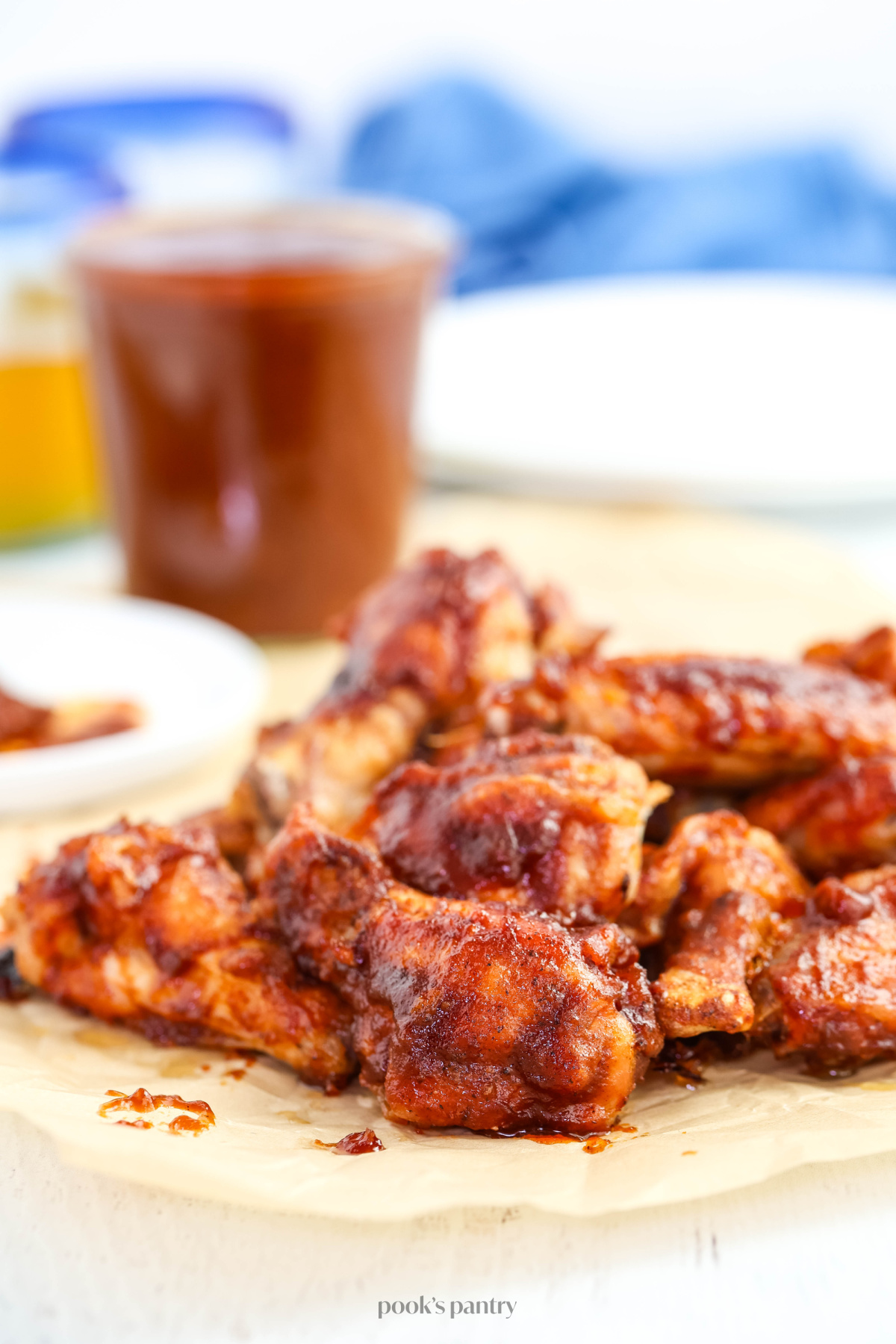 Chicken wings with BBQ sauce on a piece of brown parchment paper. There is a jar of BBQ sauce in the background.