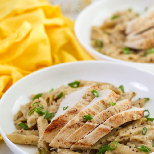 One pan chicken Dijon pasta garnished with scallions in a shallow, white bowl.