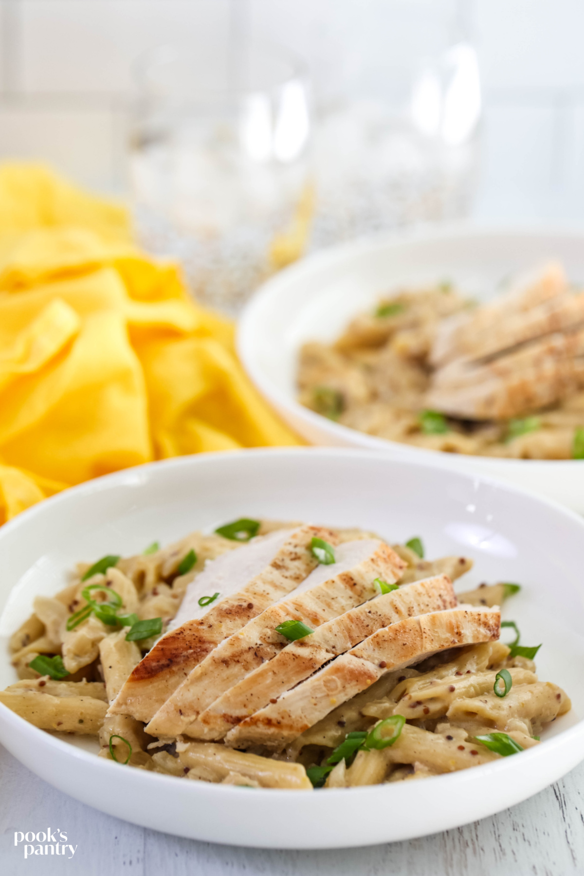 Sliced chicken breast on top of creamy Dijon pasta in a white bowl.