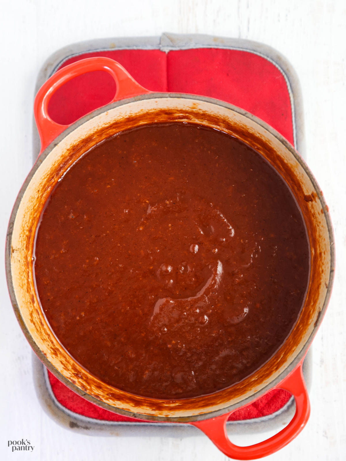 Maple BBQ sauce in a red Dutch oven pot sitting on a red pot holder.