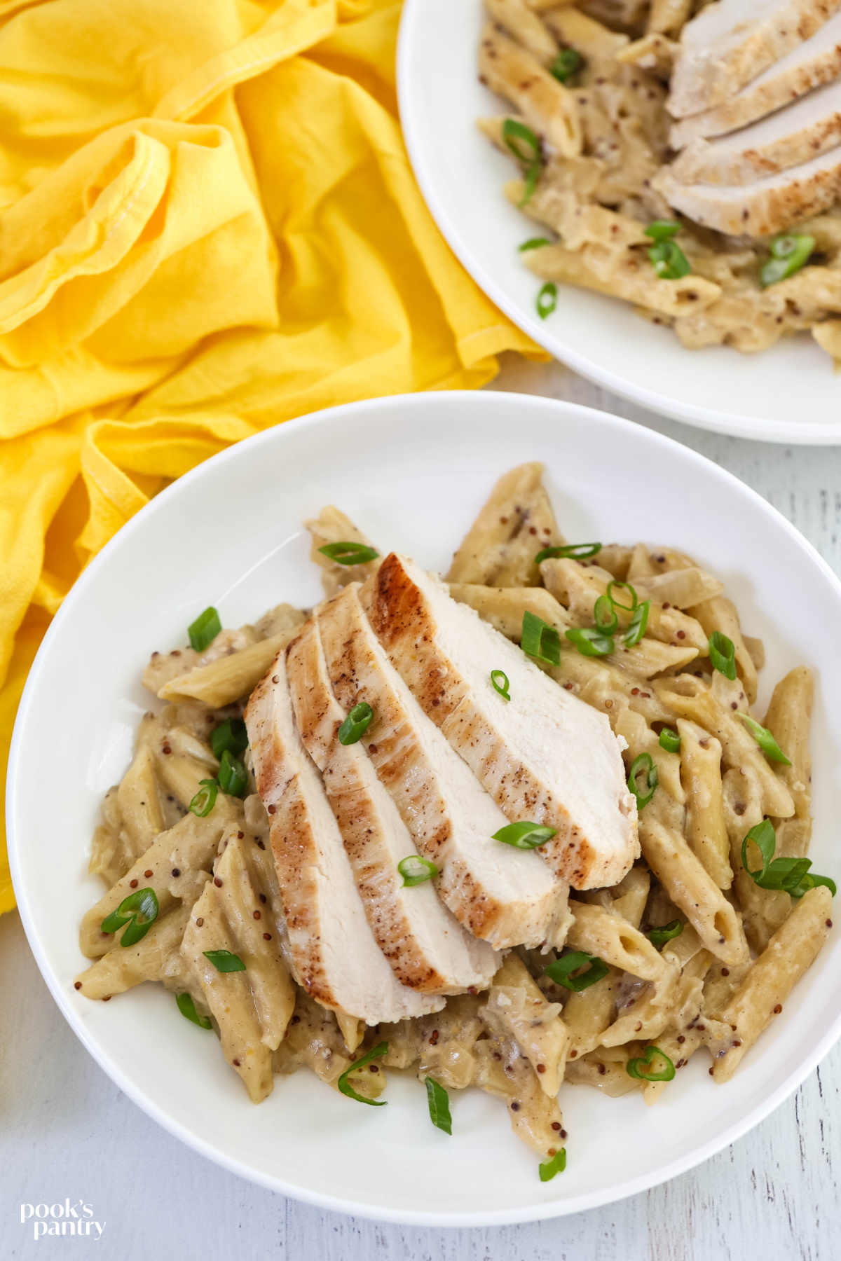 Chicken and pasta in a white bowl with a yellow towel in the background.