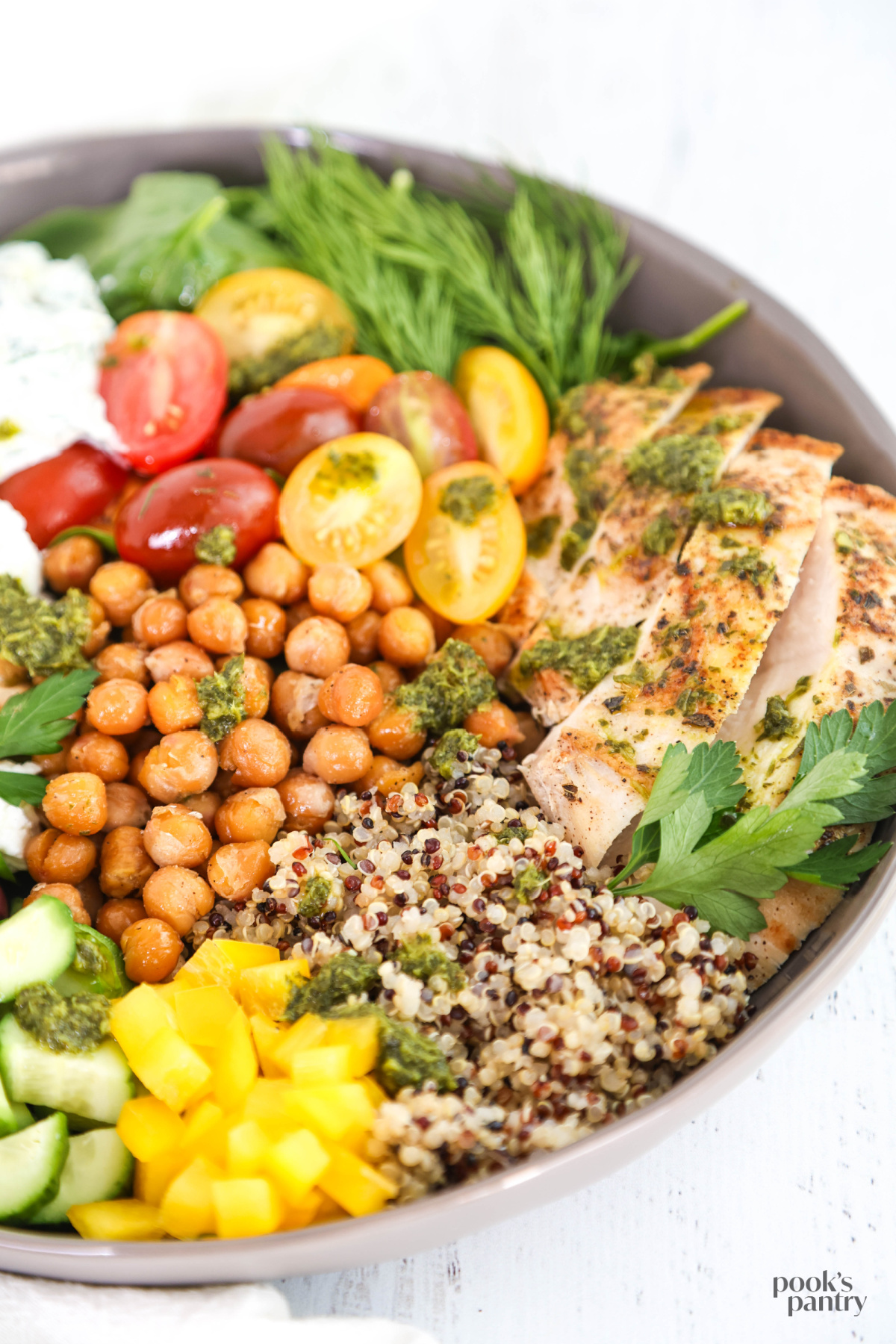Close up view of ingredients in a gray shallow bowl, dotted with gremolata sauce and fresh herbs.
