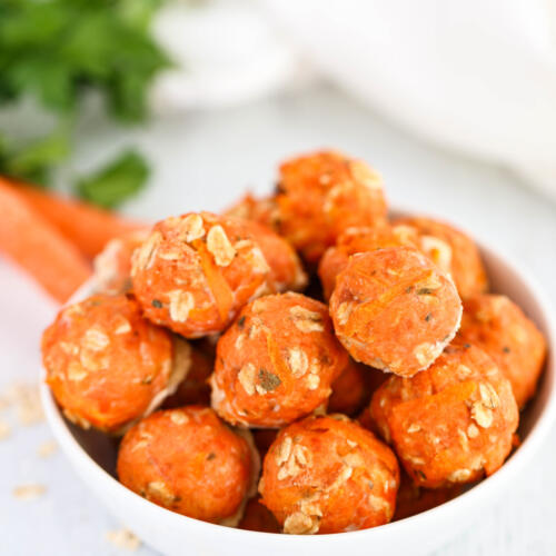 Salmon meatballs for dogs in a small white bowl with ingredients in the background.