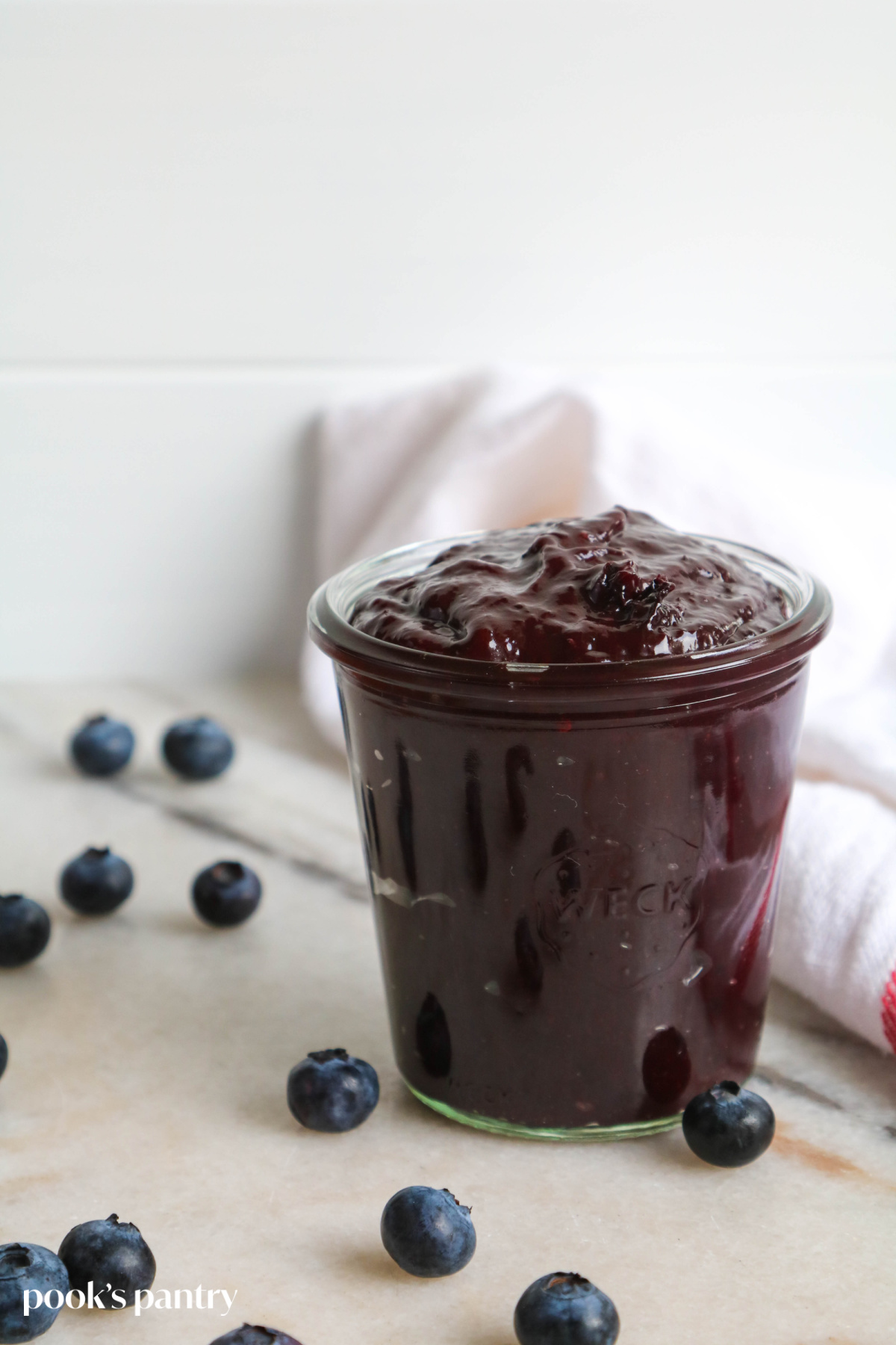 Blueberry BBQ sauce in a glass jar on a white marble background.