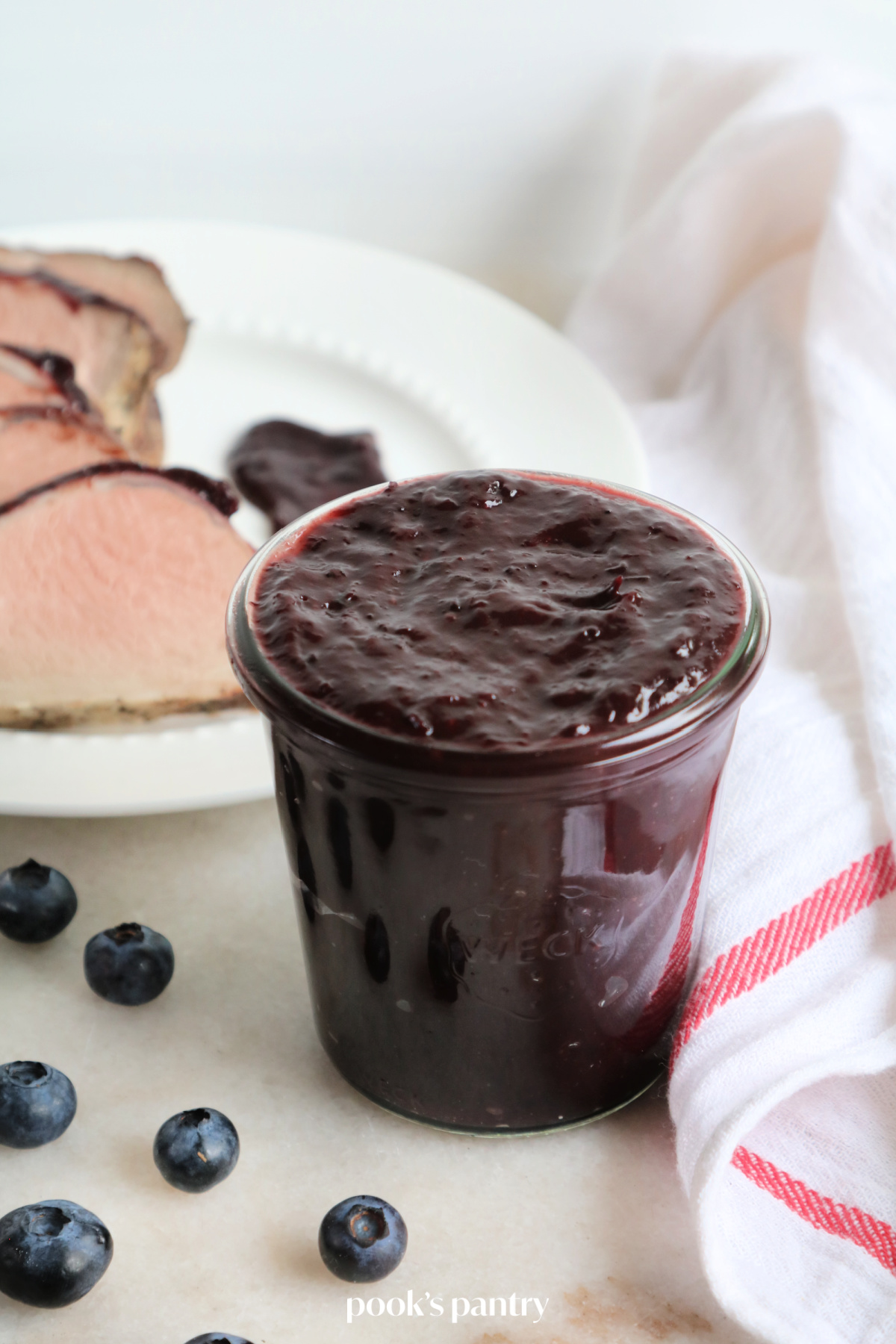 A plate of sliced pork with a jar of blueberry BBQ sauce sitting in front of the plate of pork.