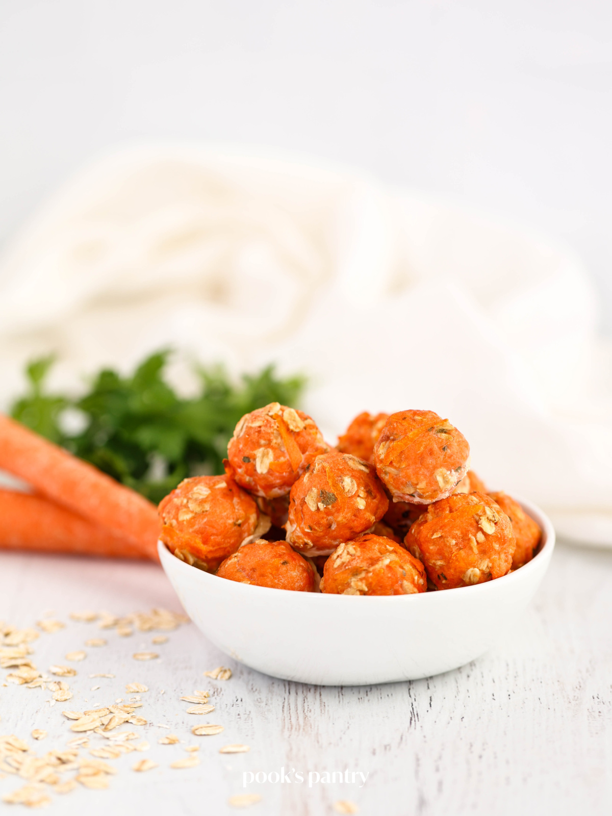 Salmon dog treats in a small white bowl with carrots and parsley in the background.