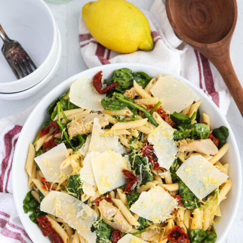 Spinach artichoke pasta salad tossed with a light lemon sauce and shaved parmesan in a white serving bowl.