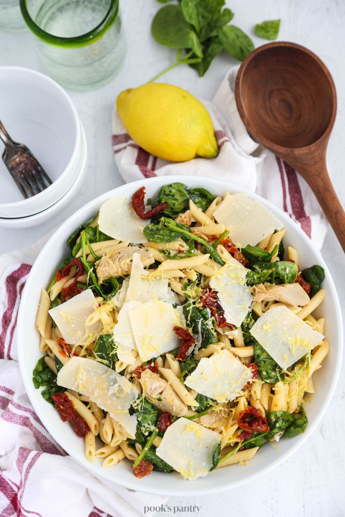 Spinach artichoke pasta salad tossed with a light lemon sauce and shaved parmesan in a white serving bowl.