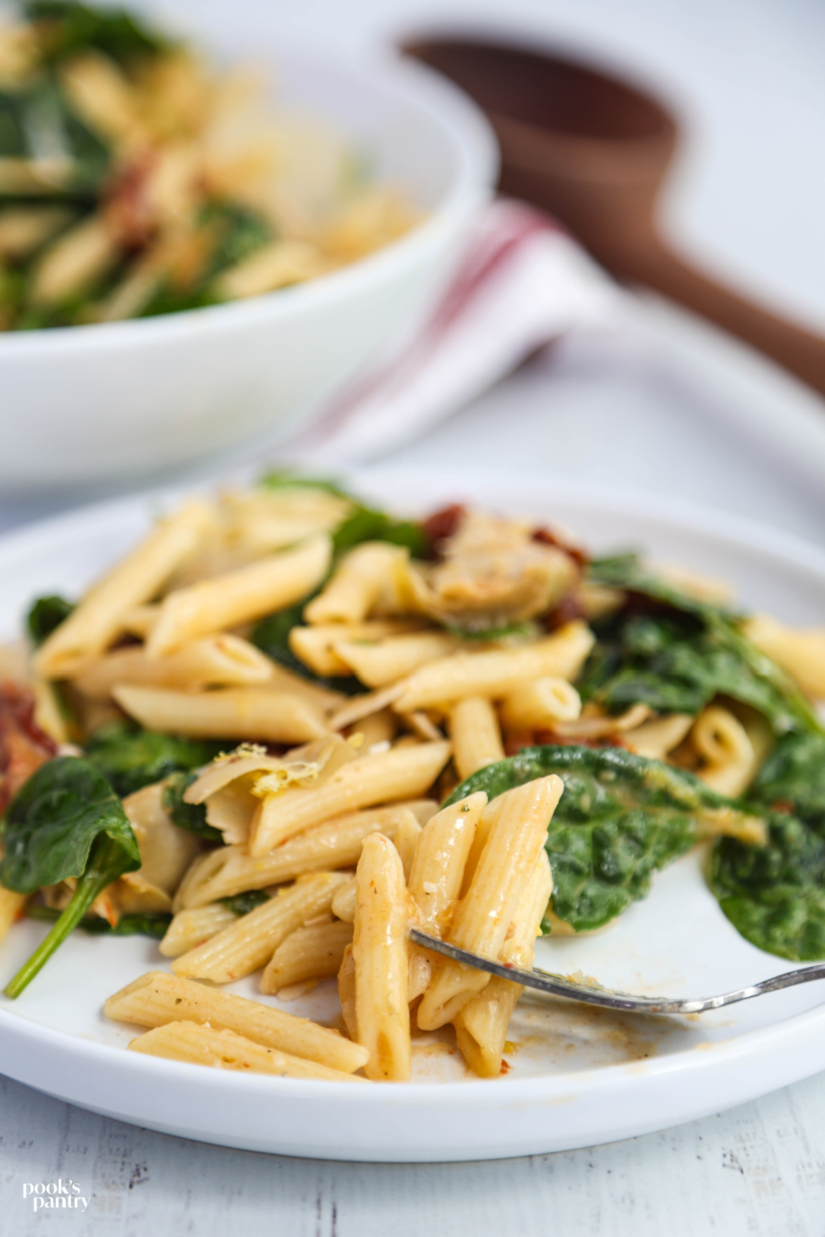 Close-up of spinach artichoke pasta salad on a fork, showing pasta coated in a light lemon dressing with parmesan.