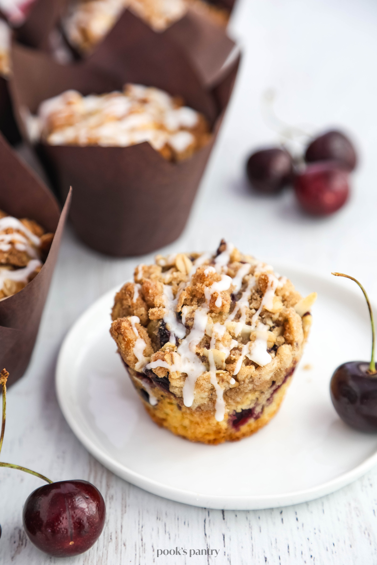Close up photo of a fresh cherry muffin on a small white plate, showing the texture of the streusel topping.