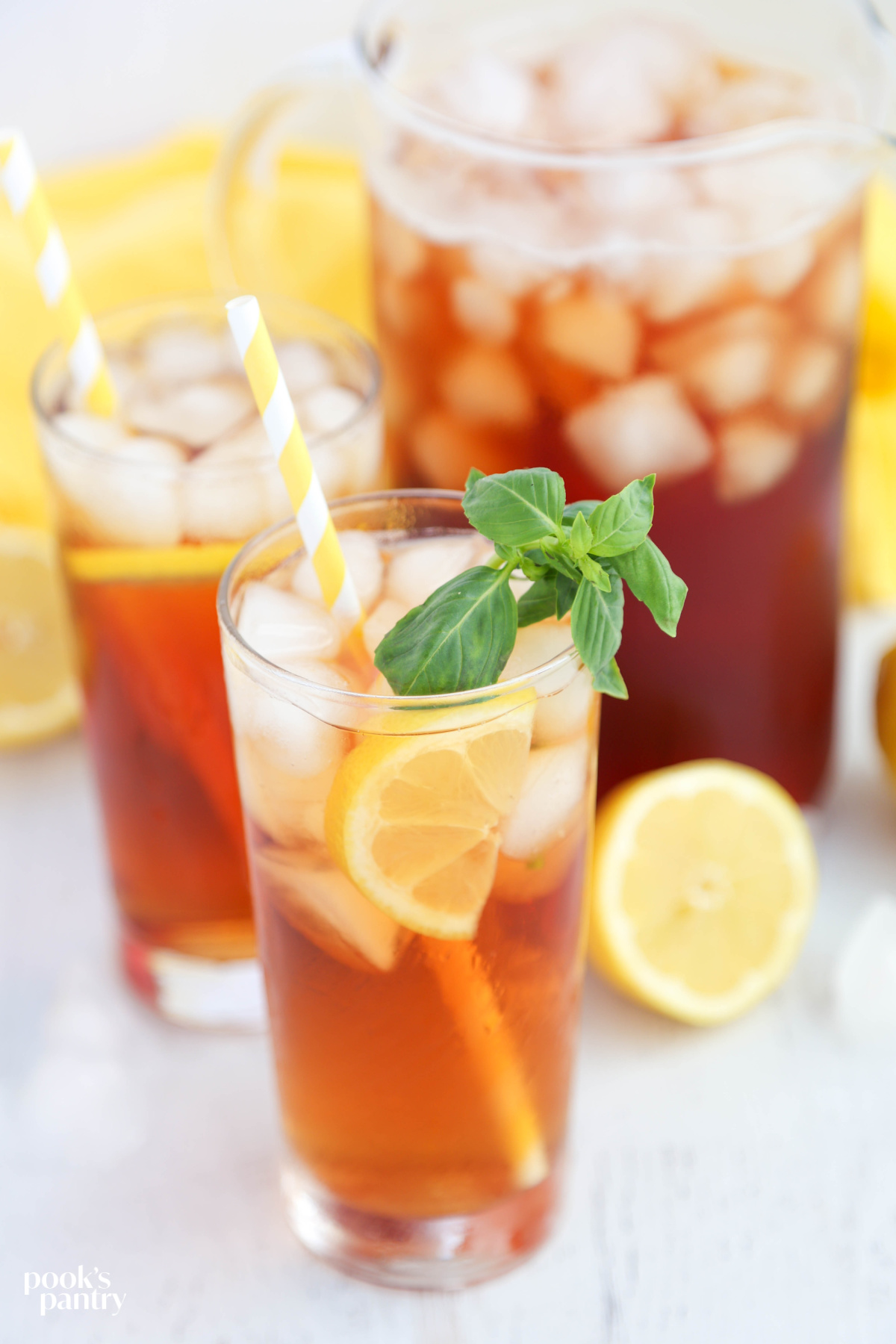 Glass of iced tea with basil and lemon. There is a yellow and white striped straw in the glass.