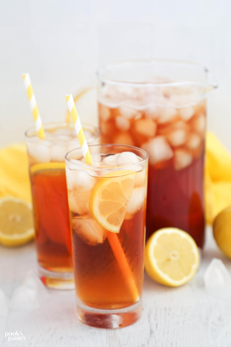 Two glasses of lemonade sun tea with a pitcher of tea in the background. There are yellow and white striped straws in the glasses.
