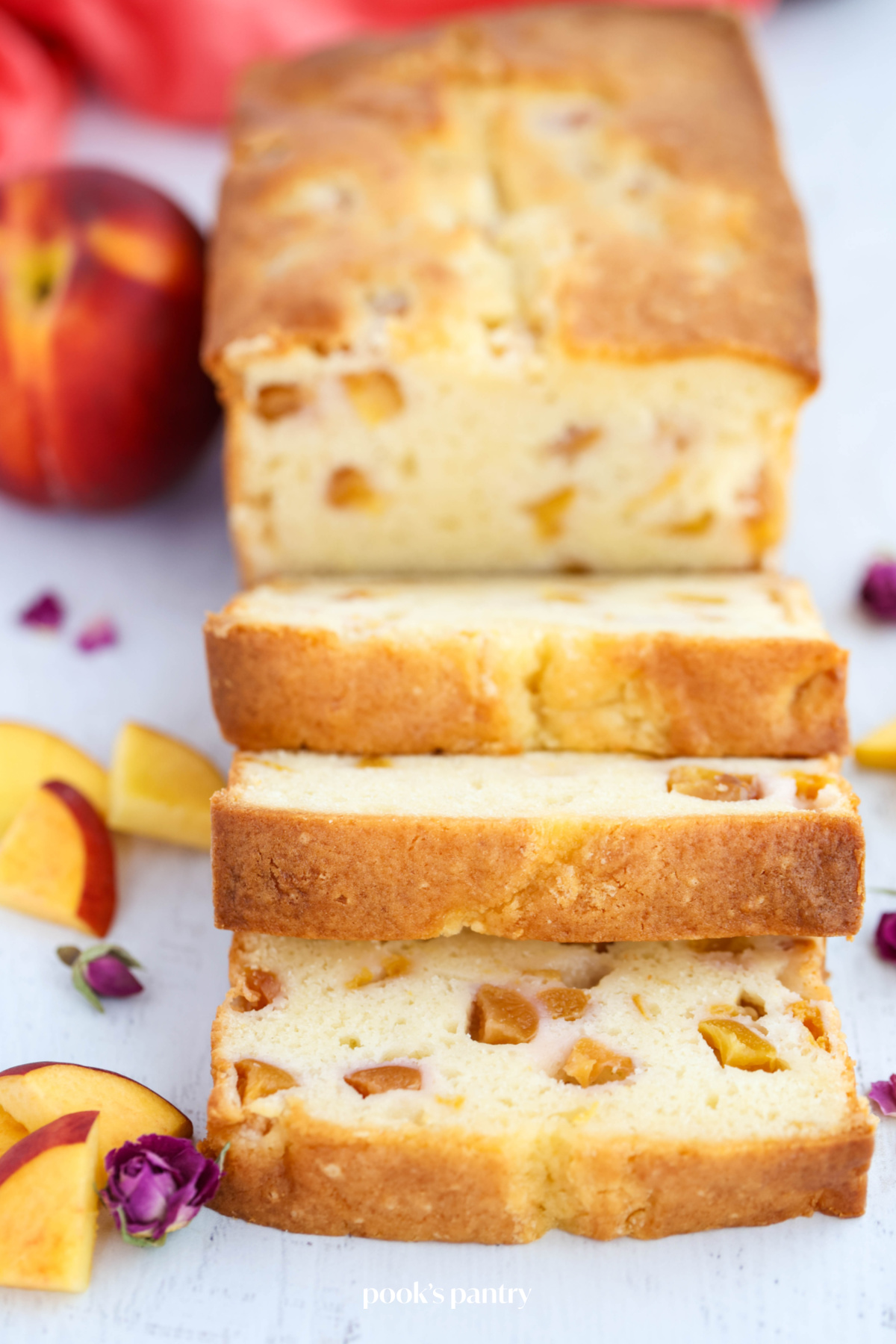 Slices of peach pound cake on a light gray background, with a dried rosebud and slices of peach in the bottom left corner of  the photo.