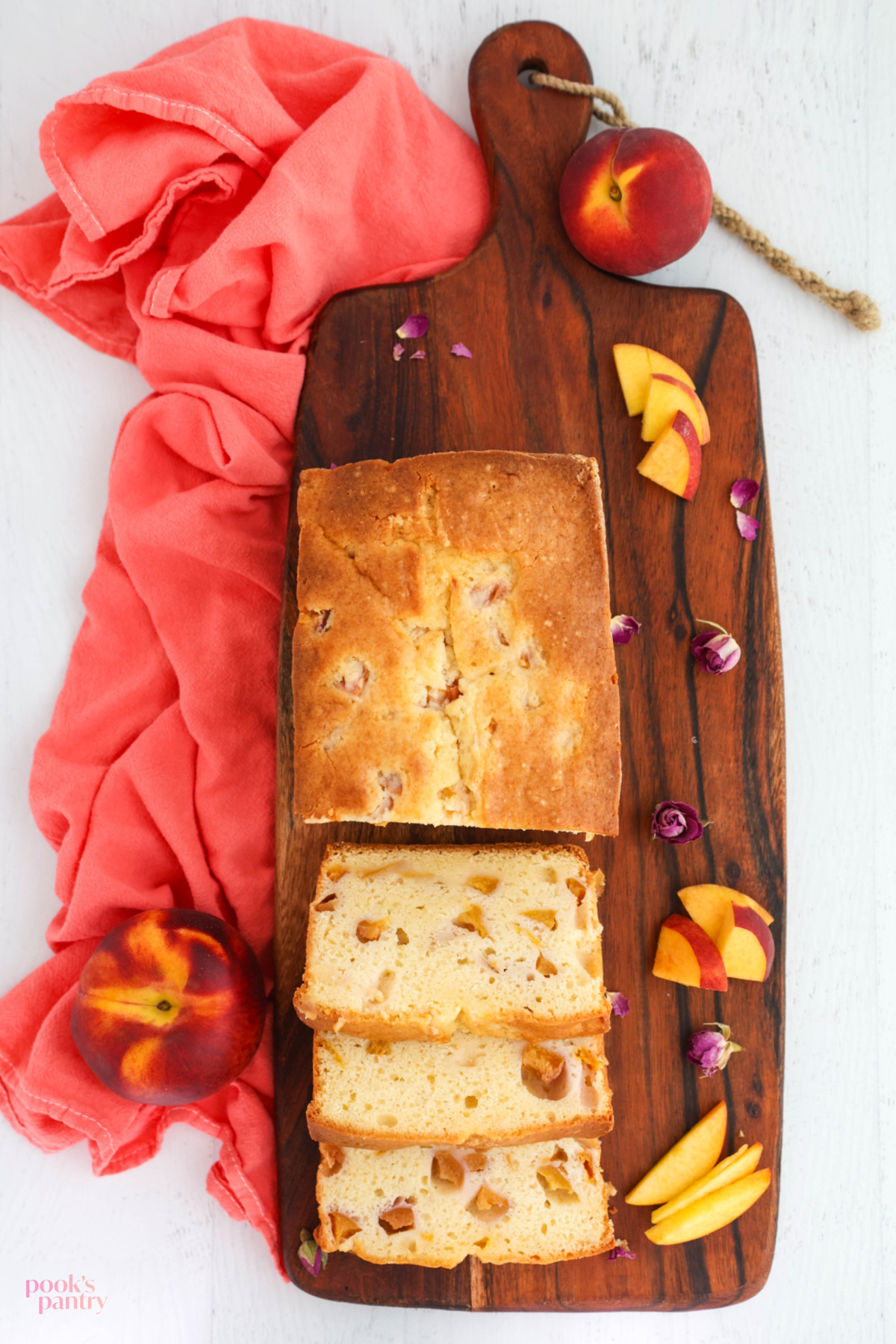 Peaches and cream loaf cake on a brown wooden cutting board, with a coral colored dish towel on the side.